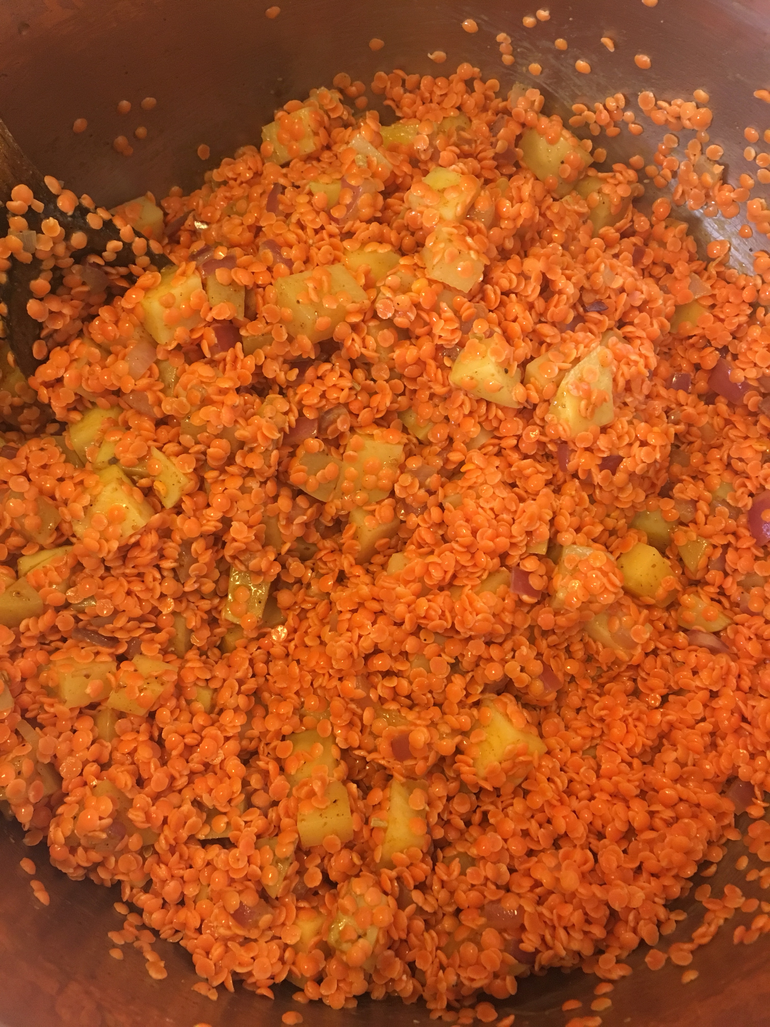 Photo of red lentils and potatoes being sauteed in a pot.