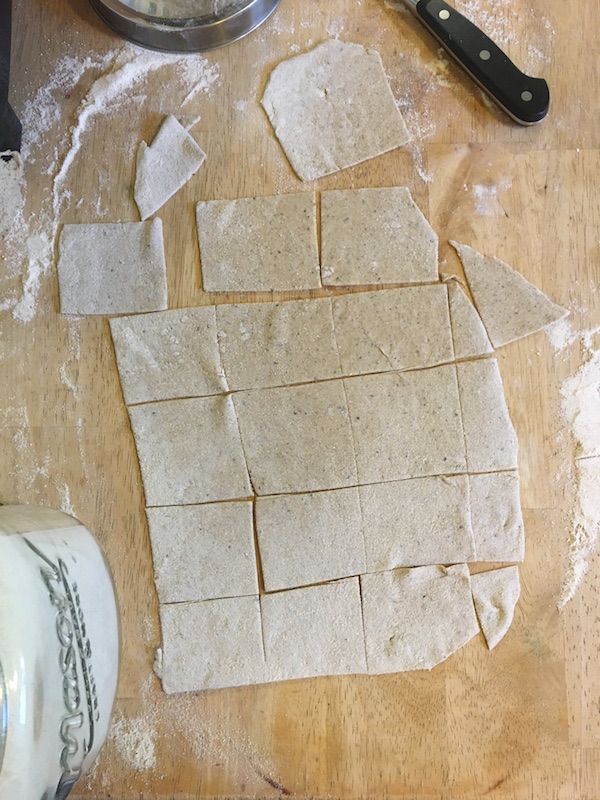 Eggless vegan pasta dough with black pepper. Large flat square pasta sheets cut and sitting on a table. Wusthof paring knife, steel can, jar of flour and extra flour surrounds pasta.