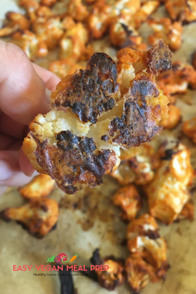 Photo showing depicting doneness of baked cauliflower. A hand holding up a baked cauliflower floret. easyveganmealprep.com